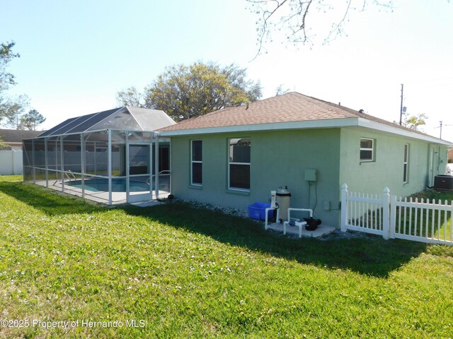 back of property with stucco siding, a lawn, glass enclosure, and fence