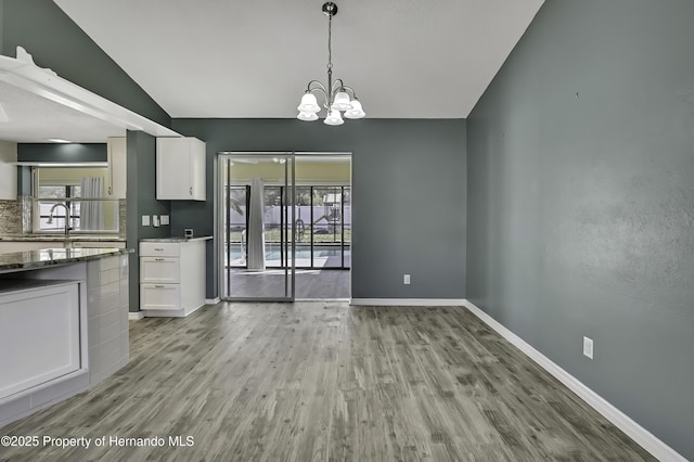 unfurnished dining area with plenty of natural light, baseboards, a notable chandelier, and light wood-style flooring