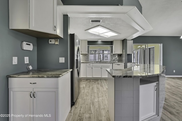 kitchen featuring a sink, decorative backsplash, stainless steel fridge, light wood-style flooring, and white cabinets