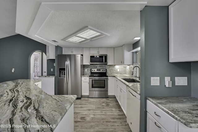 kitchen with light stone counters, a sink, arched walkways, light wood-style flooring, and appliances with stainless steel finishes