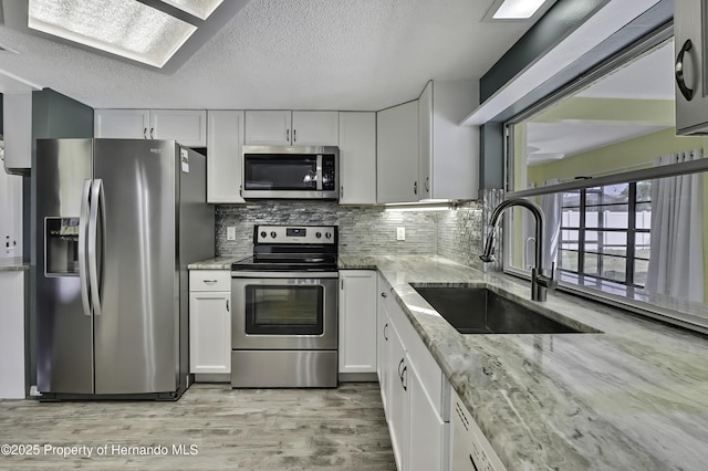 kitchen with white cabinets, stainless steel appliances, a sink, light wood-style floors, and light stone countertops