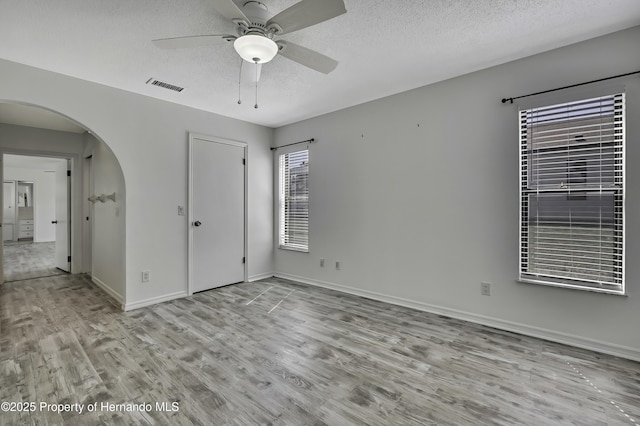 unfurnished bedroom with wood finished floors, a textured ceiling, arched walkways, baseboards, and visible vents