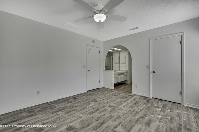 unfurnished bedroom with arched walkways, wood finished floors, visible vents, and baseboards