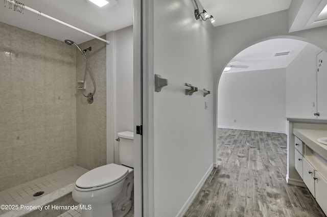 full bath with tiled shower, visible vents, a ceiling fan, wood finished floors, and vanity