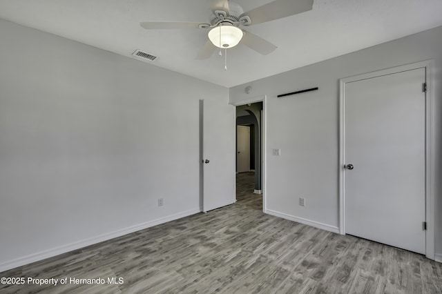 unfurnished bedroom featuring wood finished floors, visible vents, a ceiling fan, arched walkways, and baseboards