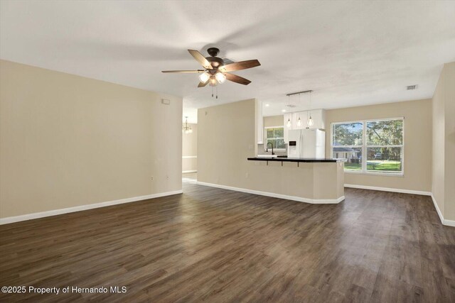 unfurnished living room with visible vents, dark wood-type flooring, a sink, baseboards, and ceiling fan