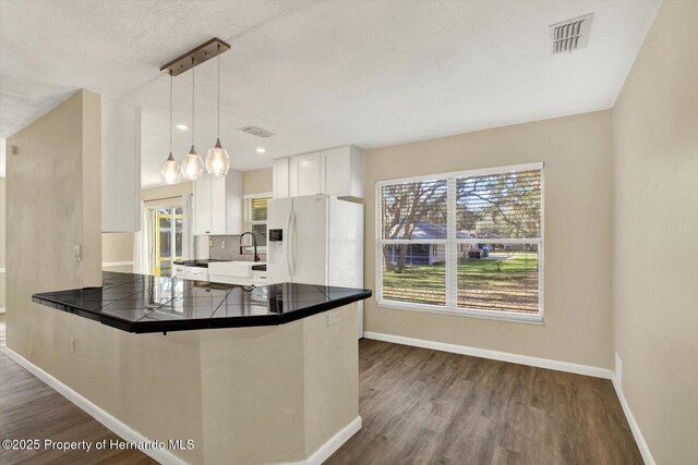 kitchen with baseboards, visible vents, a peninsula, white refrigerator with ice dispenser, and white cabinetry