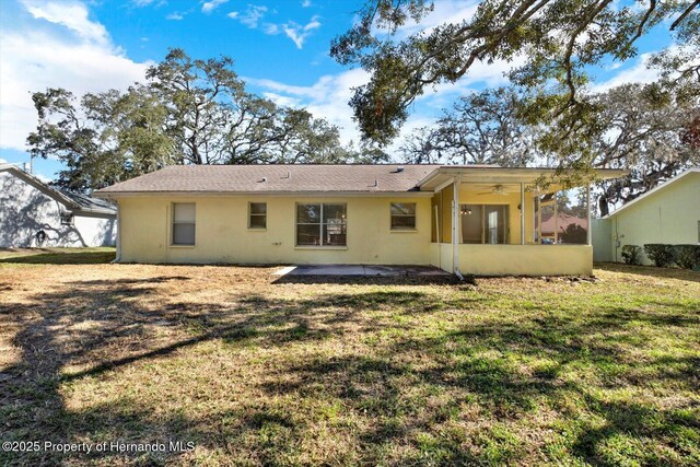 back of property with a ceiling fan, a patio area, a lawn, and stucco siding