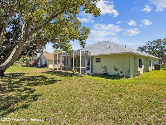 back of house featuring central AC unit, roof with shingles, a yard, stucco siding, and a lanai