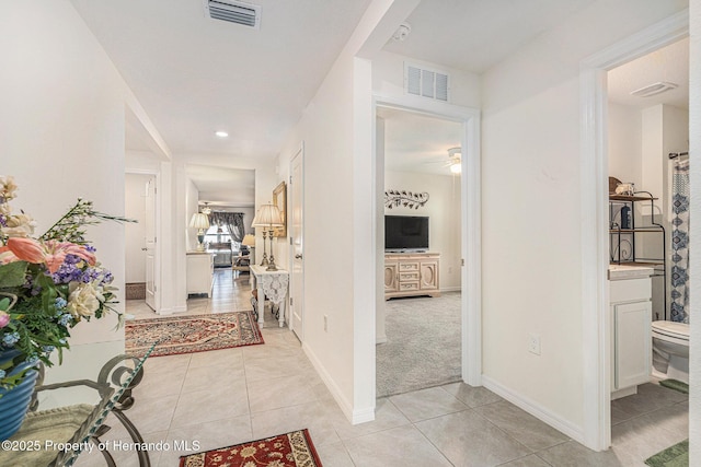 hallway featuring light tile patterned floors, baseboards, and visible vents