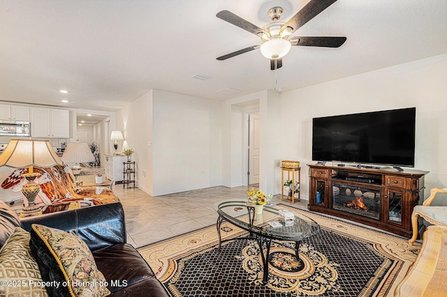 living area featuring visible vents, baseboards, light tile patterned floors, a glass covered fireplace, and a ceiling fan