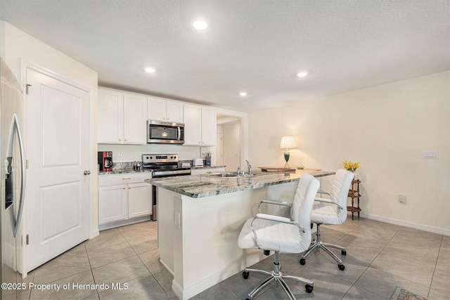 kitchen featuring light stone countertops, a kitchen bar, white cabinets, stainless steel appliances, and a sink