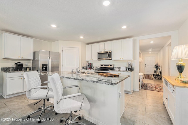 kitchen with a kitchen island with sink, a sink, light stone counters, white cabinetry, and stainless steel appliances