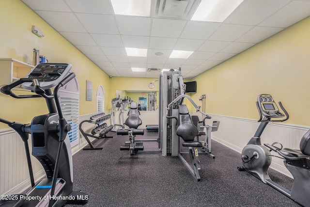 exercise room with a paneled ceiling, visible vents, and wainscoting