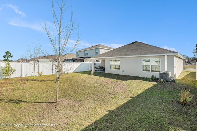 back of house featuring central AC unit, a lawn, a fenced backyard, and stucco siding