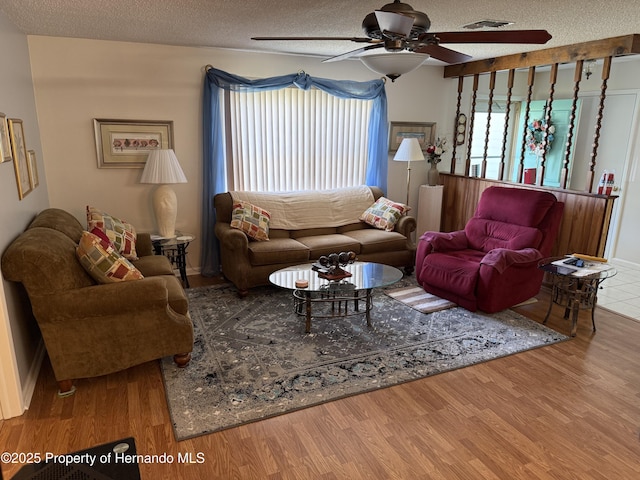 living room with a ceiling fan, wood finished floors, visible vents, and a textured ceiling