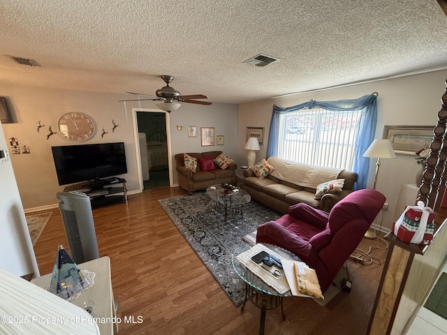 living room featuring ceiling fan, visible vents, a textured ceiling, and wood finished floors