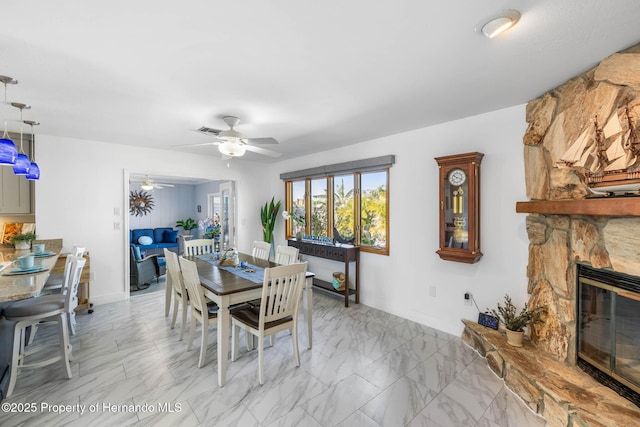 dining area featuring a stone fireplace, a ceiling fan, visible vents, and marble finish floor