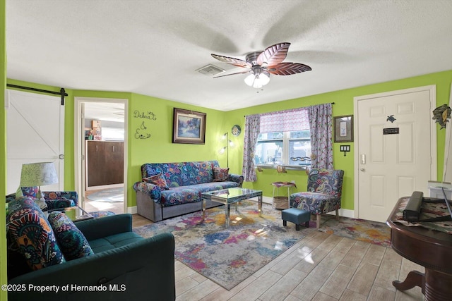 living area featuring visible vents, a healthy amount of sunlight, a barn door, and ceiling fan