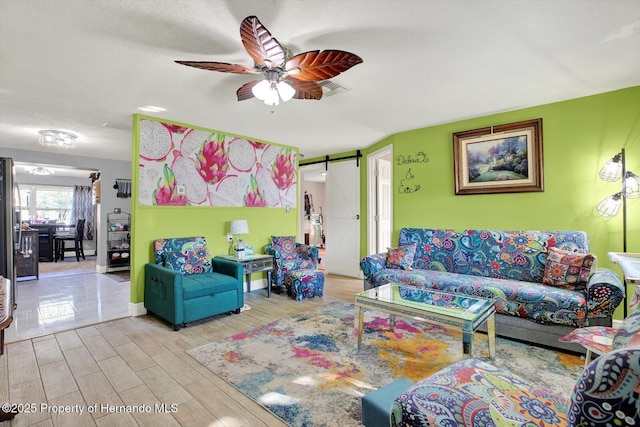 living area with a barn door, visible vents, wood finished floors, and a ceiling fan