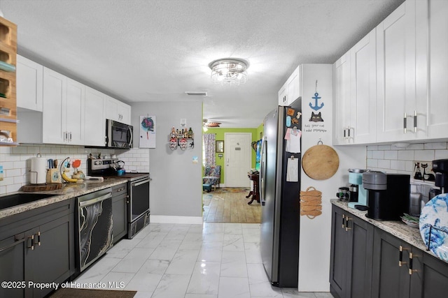 kitchen featuring marble finish floor, a textured ceiling, white cabinetry, stainless steel appliances, and baseboards