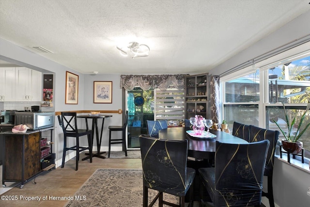 dining room with baseboards, light wood-style floors, visible vents, and a textured ceiling