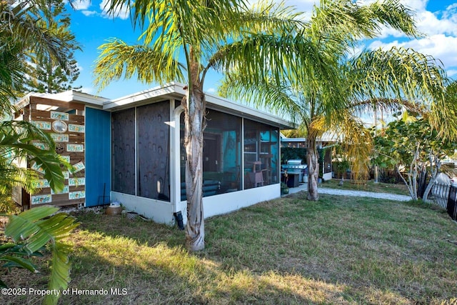 view of side of home featuring a lawn, fence, and a sunroom