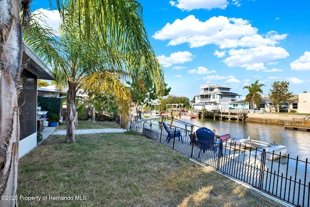 view of yard featuring fence, a water view, and a boat dock