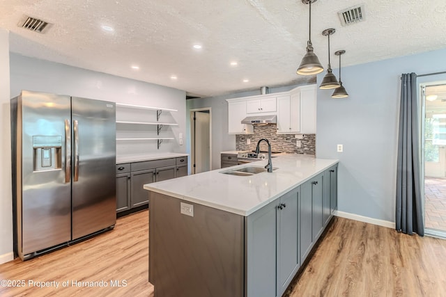 kitchen with a sink, backsplash, under cabinet range hood, stainless steel refrigerator with ice dispenser, and open shelves