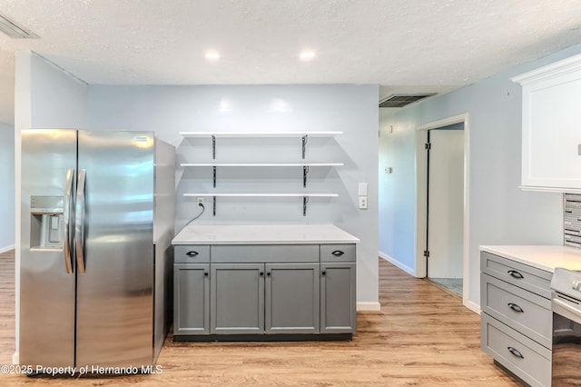 kitchen featuring visible vents, gray cabinetry, open shelves, stainless steel fridge, and light wood finished floors