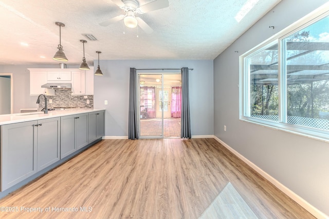 interior space with visible vents, gray cabinets, under cabinet range hood, backsplash, and baseboards