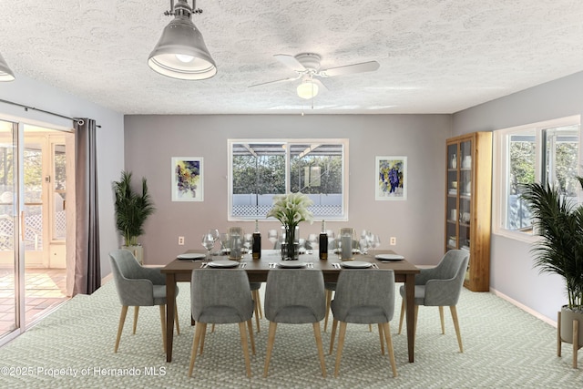 dining area with a ceiling fan, light colored carpet, baseboards, and a textured ceiling
