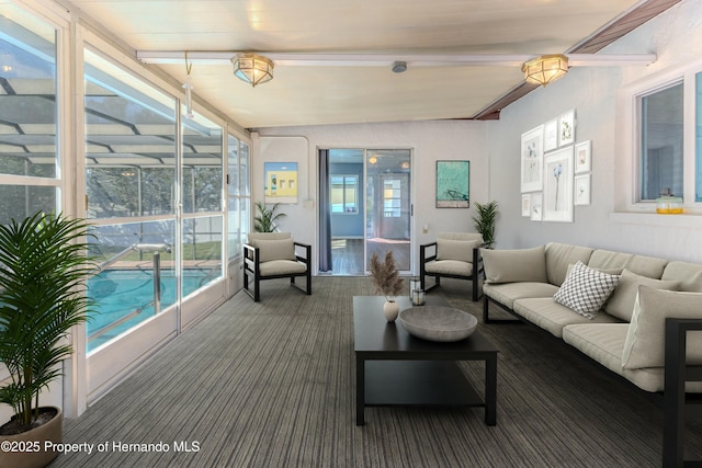 carpeted living area with a healthy amount of sunlight, expansive windows, vaulted ceiling with beams, and a sunroom