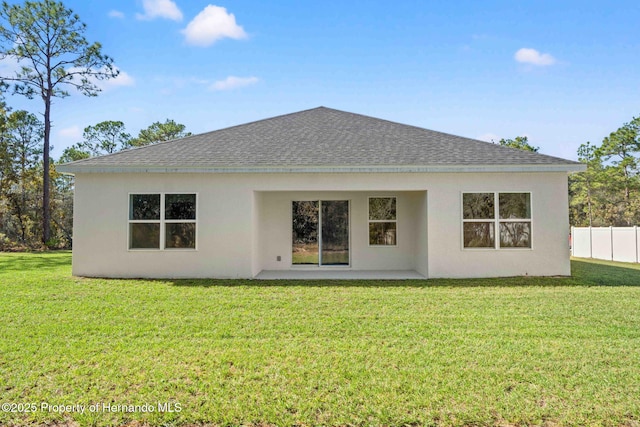 back of house featuring stucco siding, fence, a lawn, and a shingled roof