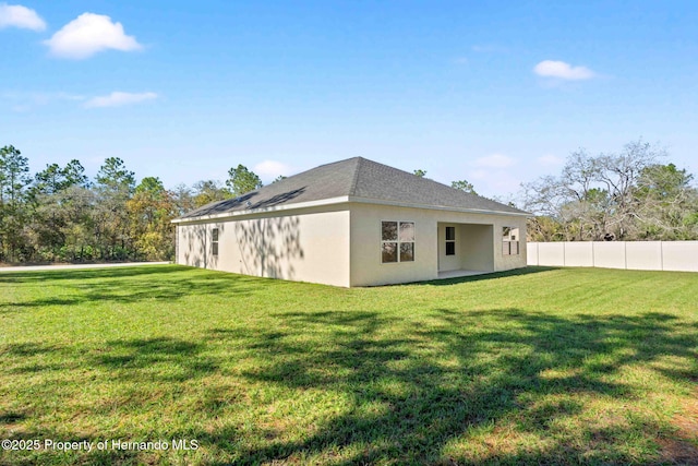 back of house with stucco siding, a yard, and fence