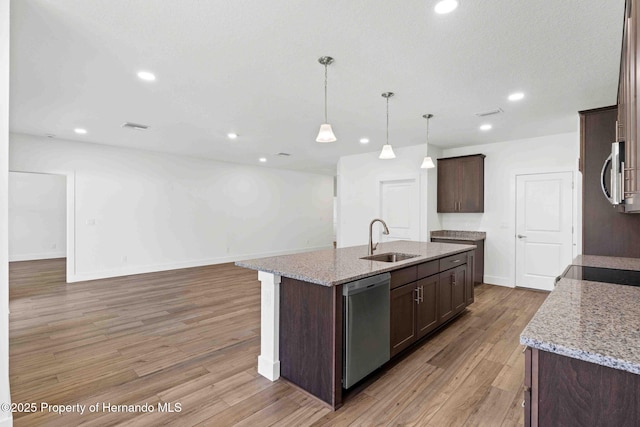 kitchen featuring dark brown cabinetry, an island with sink, appliances with stainless steel finishes, light wood-style floors, and a sink