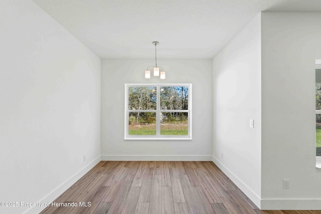 unfurnished dining area featuring a chandelier, baseboards, and wood finished floors