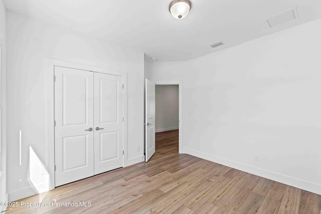 unfurnished bedroom featuring visible vents, baseboards, a closet, and light wood-style flooring