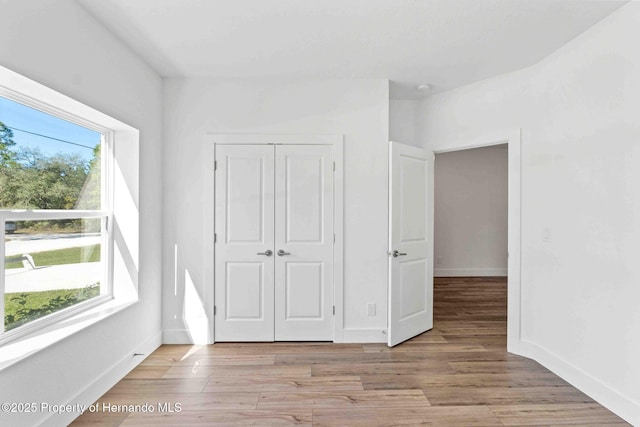 unfurnished bedroom with a closet, baseboards, and light wood-style floors