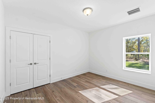 unfurnished bedroom featuring wood finished floors, visible vents, a closet, and baseboards