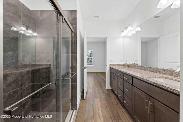 bathroom with a sink, wood finished floors, a stall shower, and double vanity