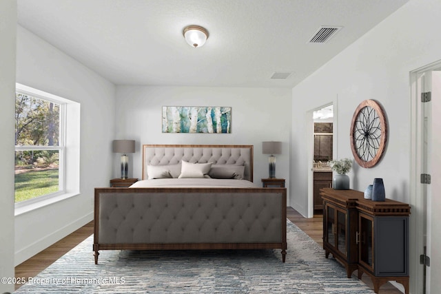 bedroom with wood finished floors, visible vents, ensuite bathroom, and baseboards