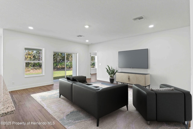 living room with recessed lighting, visible vents, baseboards, and wood finished floors