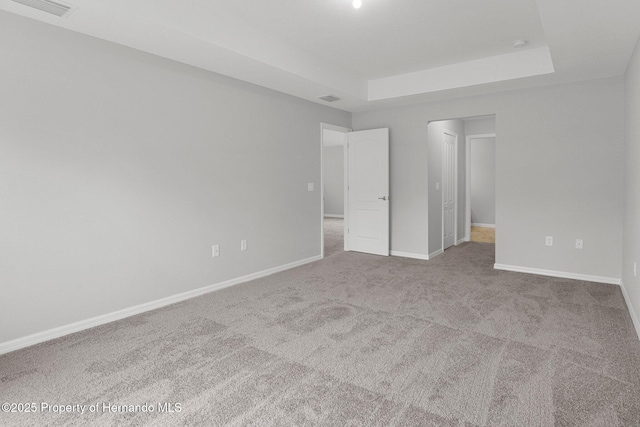 unfurnished bedroom featuring a tray ceiling, visible vents, baseboards, and carpet floors