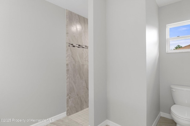 full bathroom with toilet, baseboards, and tiled shower