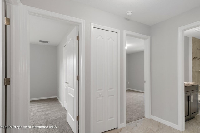 hall with visible vents, baseboards, and light colored carpet