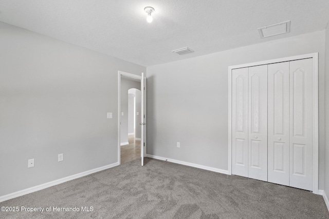 unfurnished bedroom featuring visible vents, baseboards, carpet flooring, a closet, and a textured ceiling