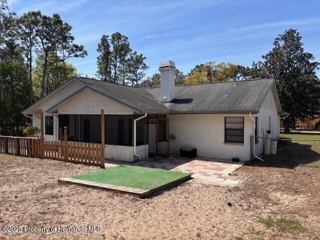 back of house featuring fence, roof with shingles, a chimney, a sunroom, and a patio area