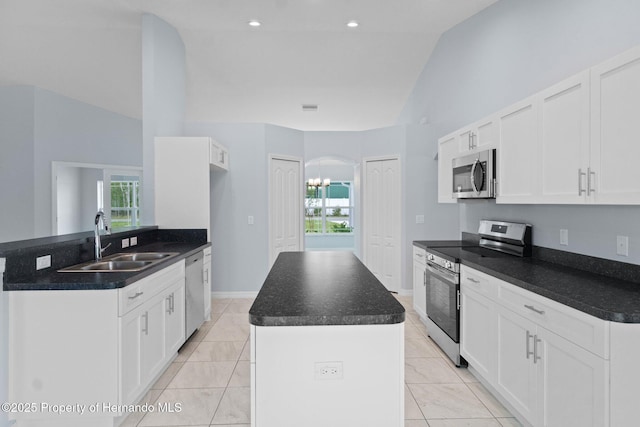 kitchen featuring a center island with sink, a sink, stainless steel appliances, vaulted ceiling, and dark countertops