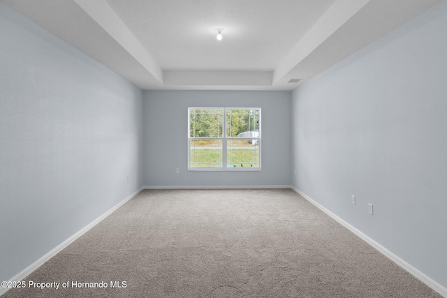 carpeted empty room featuring a tray ceiling, visible vents, and baseboards